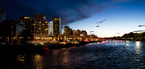 Downtown Calgary east village skyline at twilight panorama background. Skyscraper lights reflecting in the Bow River waterfront at night wallpaper. Night view of urban city