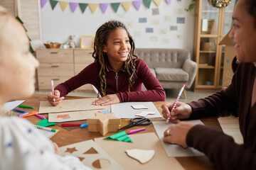 Portrait of smiling African-American girl looking at female teacher while enjoying art and craft...