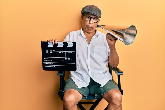 Handsome mature director man holding video film clapboard and louder depressed and worry for distress, crying angry and afraid. sad expression.