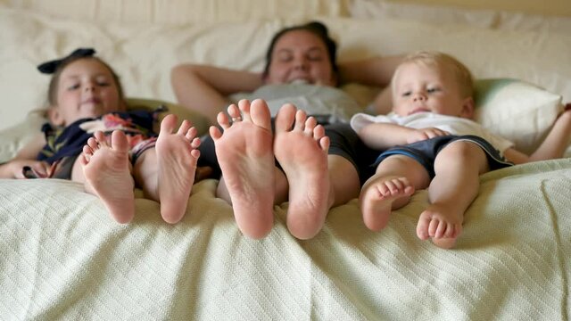 Mom and kids on bed wiggling their bare feet. Angle shot of mom with her kids wiggling their bare feet.