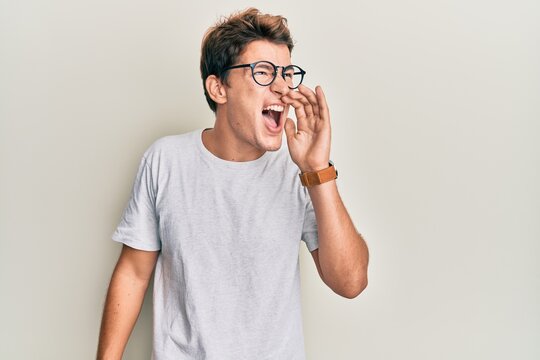 Handsome caucasian man wearing casual clothes and glasses shouting and screaming loud to side with hand on mouth. communication concept.
