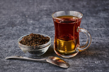 View of tea cup with sieve next to socket with brew and teaspoon on grey background
