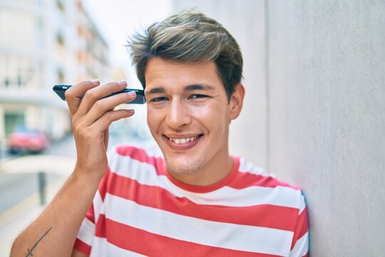 Young caucasian man smiling happy listening audio message using smartphone at the city.