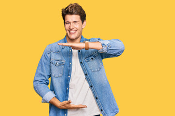 Naklejka premium Handsome caucasian man wearing casual denim jacket gesturing with hands showing big and large size sign, measure symbol. smiling looking at the camera. measuring concept.
