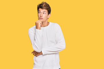 Handsome caucasian man wearing casual white sweater with hand on chin thinking about question, pensive expression. smiling with thoughtful face. doubt concept.