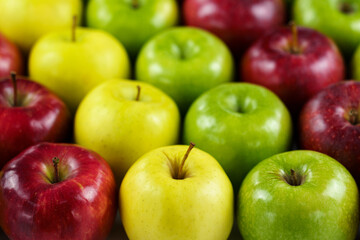Grupo de manzanas de diferentes colores y variedades dispuestas en fila con desenfoque del fondo.