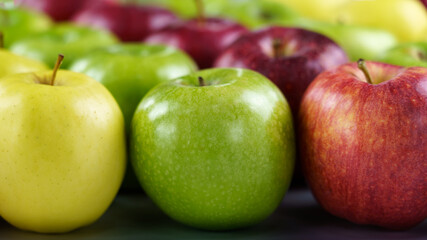 Grupo de manzanas de diferentes colores y variedades dispuestas en fila con desenfoque del fondo.