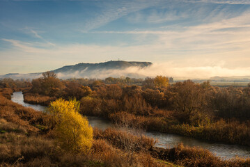 Beautiful landscape of the river bank with the autumn colors in the trees and the mist covering the mountain, Torrejón de Ardoz, Madrid, Spain