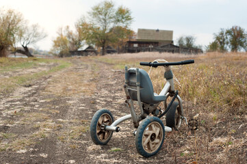 Fototapeta na wymiar old children's tricycle on a country road in the autumn.