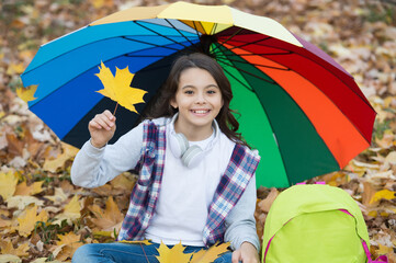 perfect autumn day of cheerful girl under colorful umbrella with school bag sitting in fall season...