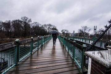 Man with umbrella crossing a bridge in the rain.