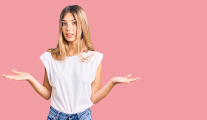 Beautiful caucasian woman with blonde hair wearing casual white tshirt clueless and confused...