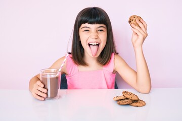 Young little girl with bang sitting on the table having breakfast sticking tongue out happy with funny expression. © Krakenimages.com