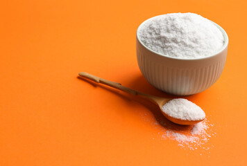 Bowl and spoon with salt on orange background, closeup. Space for text