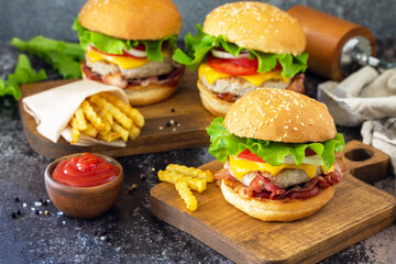 Delicious burgers with cutlet beef, bacon, french fries and ketchup on a slate table.