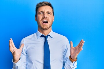 Handsome caucasian man wearing business shirt and tie crazy and mad shouting and yelling with aggressive expression and arms raised. frustration concept.