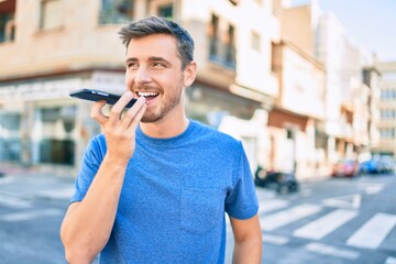 Young caucasian man smiling happy sending voice message using smartphone at the city.