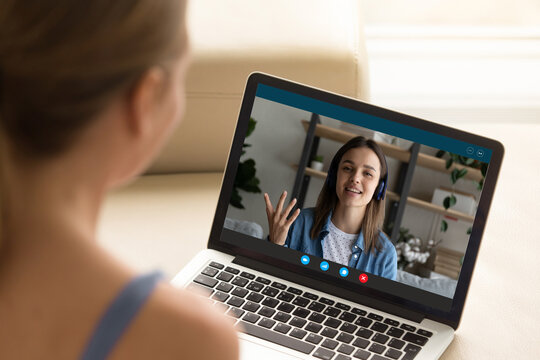 Back shoulder view of young woman enjoying web cam video call conversation with female friend in earphones or practicing foreign language online with native speaker, distant remote communication.