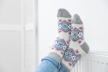Woman warming legs on heating radiator near white wall, closeup. Space for text