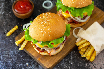 Delicious burgers with cutlet beef, bacon, french fries and ketchup on a slate table.