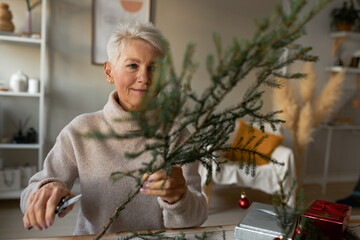 Portrait of creative senior Caucasian female in turtleneck sweater holding natural green coniferous...