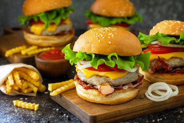 Homemade burgers with cutlet beef, cheese, bacon, french fries and ketchup on a slate table.
