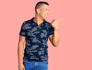 Young handsome latin man wearing casual clothes smiling with happy face looking and pointing to the side with thumb up.