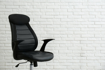Comfortable office chair near white brick wall. Space for text