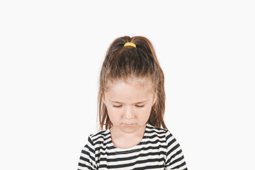 Sad girl looking down with head tilted forward down. Posing little girl wearing striped shirt. Defeat, loneliness, solitude concept.