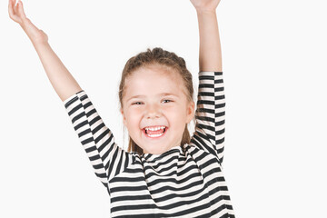 Cute laughing girl looking at camera. Happy girl with wide smile and hands up shouting Surprise, Win. Posing little girl wearing striped shirt. Celebrating concept.