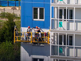 construction workers installers high-rise workers industrial climbers, painters on the lift paint the facade of the building, completion of construction of a residential building or office