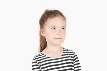 Thinking girl looking up aside.  Posing a little girl wearing a striped shirt. Girl is trying to hide something and not to look at camera. Isolated background. Secret, mystery concept.