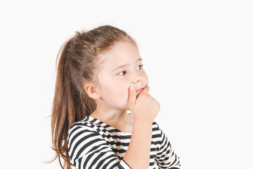 Thoughtful girl looking seriously aside and touching her chin with hand. Pensive thinking girl with eyes directed sideways on copy space. Posing little girl wearing striped shirt.