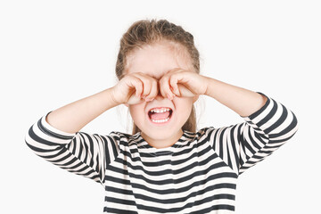 Loudly crying girl with hands covering her eyes. The upset girl is wiping tears with two hands. Posing little girl wearing a striped shirt. Negative emotion, depression, stress concept.