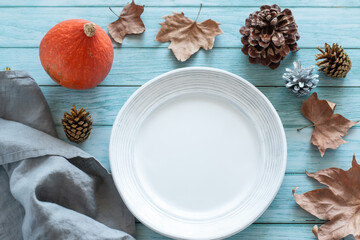 Empty plate mock up on blue wooden table with pumpkins and autumn decor, top view