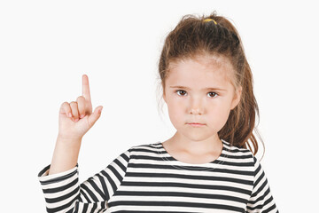 Serious girl pointing finger up, showing Number one. Posing little girl wearing a striped shirt, looking at the camera on isolated background. Advertisement and presentation concept.