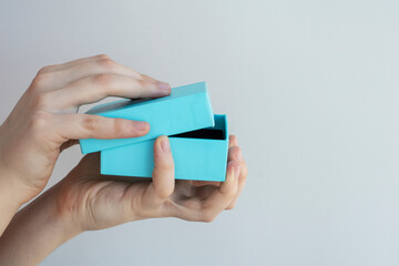 female hands hold blue square gift box and begin to open it on light background, copy space for text, greetings and presents concept
