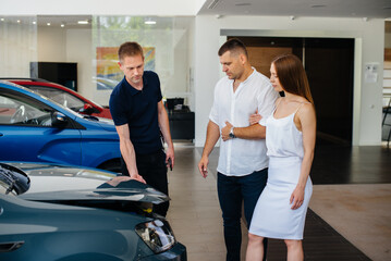 A young couple chooses a new car at the dealership and consults with a representative of the dealership. Used cars for sale. Dream fulfillment