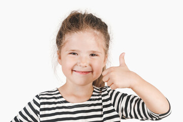 Close up portrait of happy girl looking at camera and showing thumb up. Posing little girl wearing striped shirt. Girl showing support, respect to someone. Isolated background. I like that. Good job.