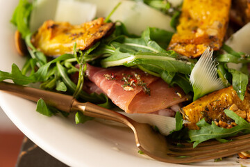 Light autumn salad with arugula, baked pumpkin, prosciutto and young parmesan, a plate of salad on a wooden table