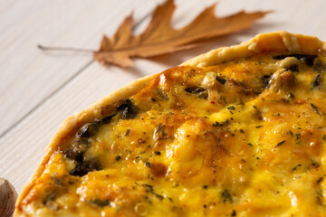 Quiche pie with mushrooms and cheese, autumn background with fallen maple and oak leaves, pine cones and hazelnuts