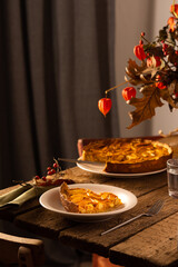 Apple pie with caramel on a wooden background, autumn bouquet in a vase, portion of pie in a plate close-up , autumn bouquet in a vase