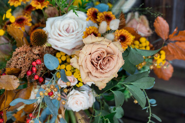 close up of fall flower arrangement with orange, beige, yellow and greenery in lush arrangement