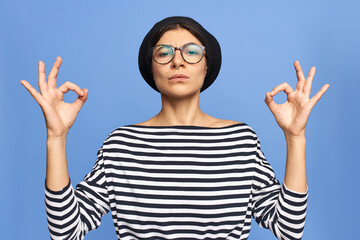 Attractive fashionable young Caucasian woman in stylish eyeglasses, beret and striped shirt showing...