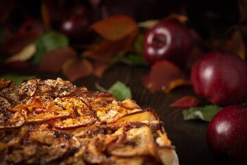 Delicious sweet pie with red apples, apple pie sprinkled with cocoa on a wooden background, rustic style, background of red leaves of grapes and ripe fruits