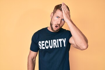 Young caucasian man wearing security t shirt surprised with hand on head for mistake, remember...