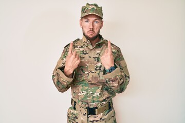 Young caucasian man wearing camouflage army uniform pointing up looking sad and upset, indicating direction with fingers, unhappy and depressed.