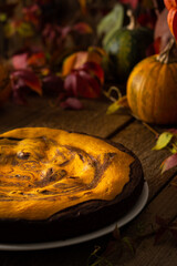 Chocolate pumpkin sweet pie on a wooden background, cake on a background of red leaves of grapes, pumpkins and autumn bouquet in a vase