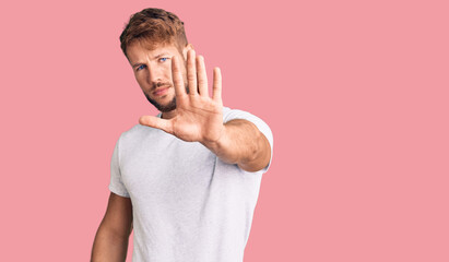 Young caucasian man wearing casual white tshirt doing stop sing with palm of the hand. warning...