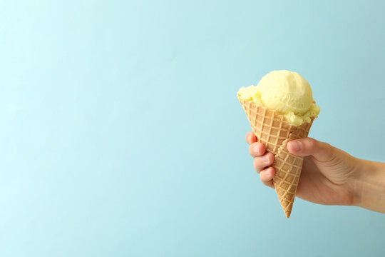 Woman holding waffle cone with delicious yellow ice cream on light blue background, closeup. Space for text